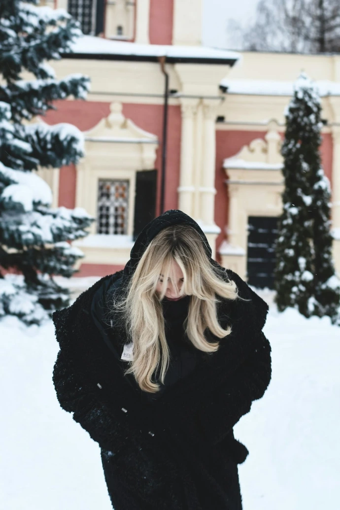 Woman in black coat in snowy park near building